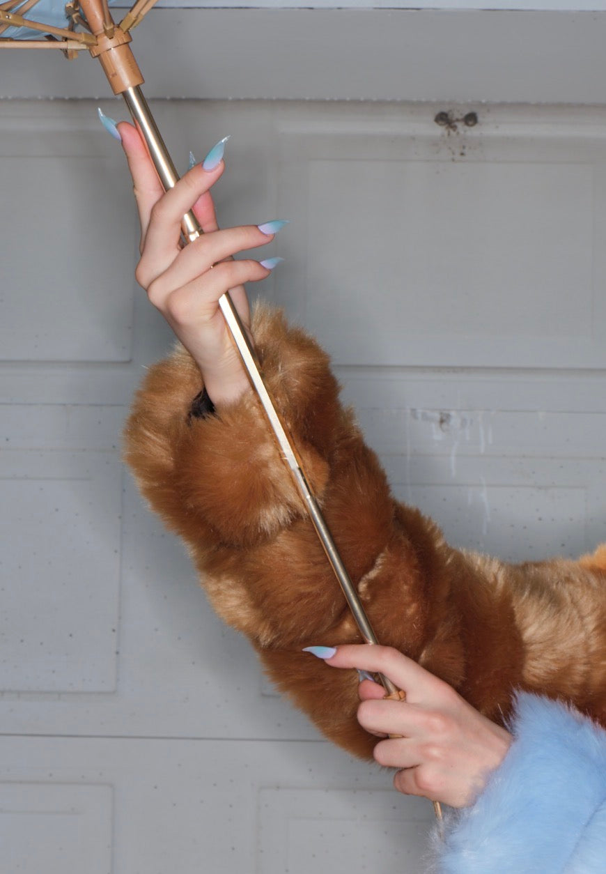 Editorial fashion photograph with hands wearing false claw nails. Nails are painted in gradient hues of aqua, lavender, and pink.