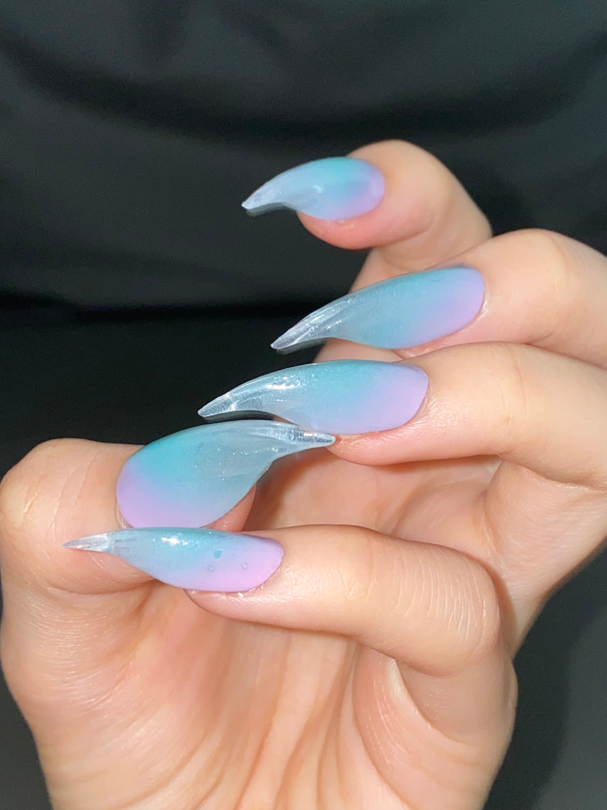 A hand wearing false claw nails, painted in gradient hues of aqua, lavender, and pink.