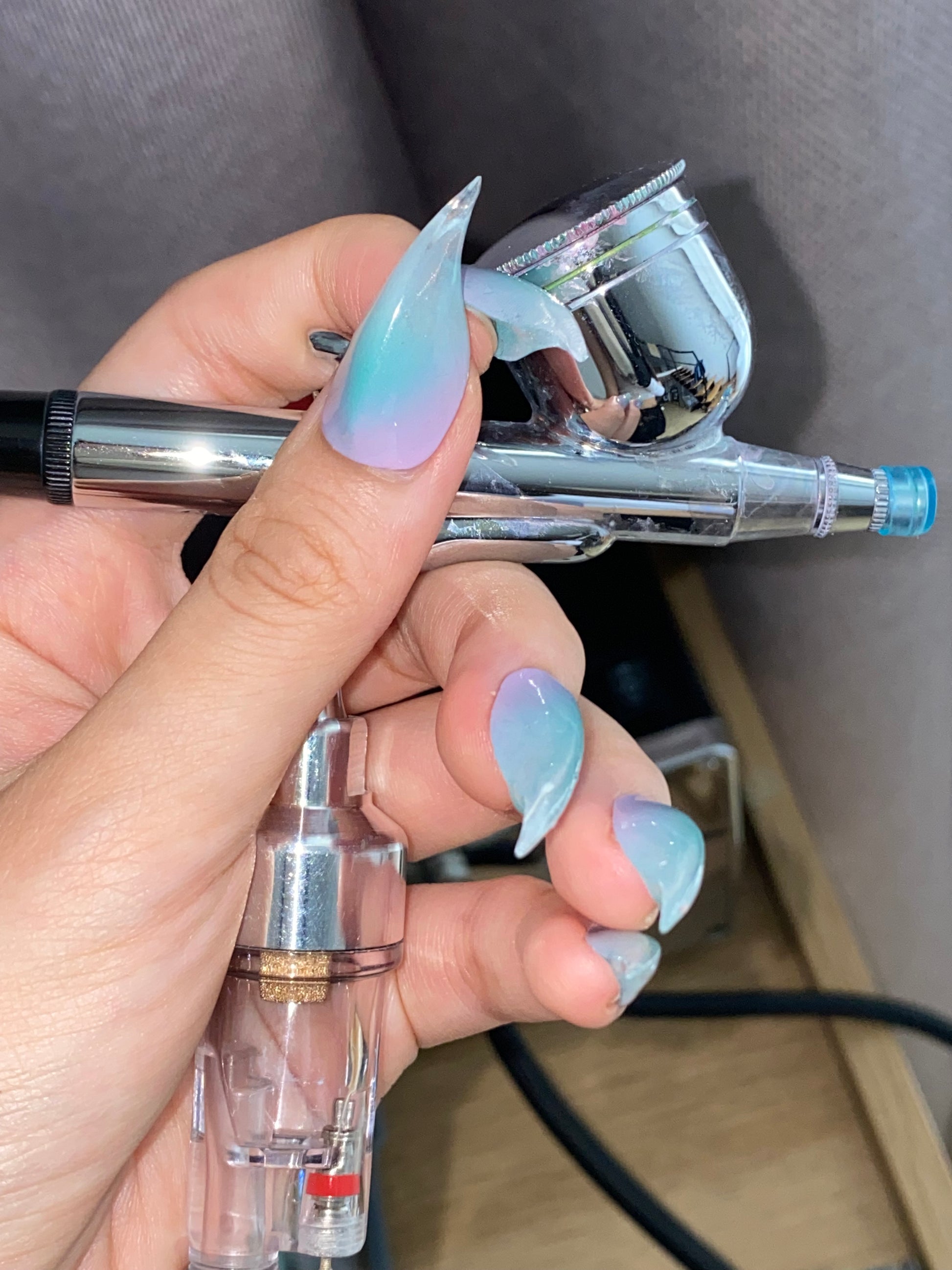 Close-up of hand wearing futuristic claw nails with translucent aqua-blue and violet gradient — glassy iridescent press-on design by NAILTER EGO.”