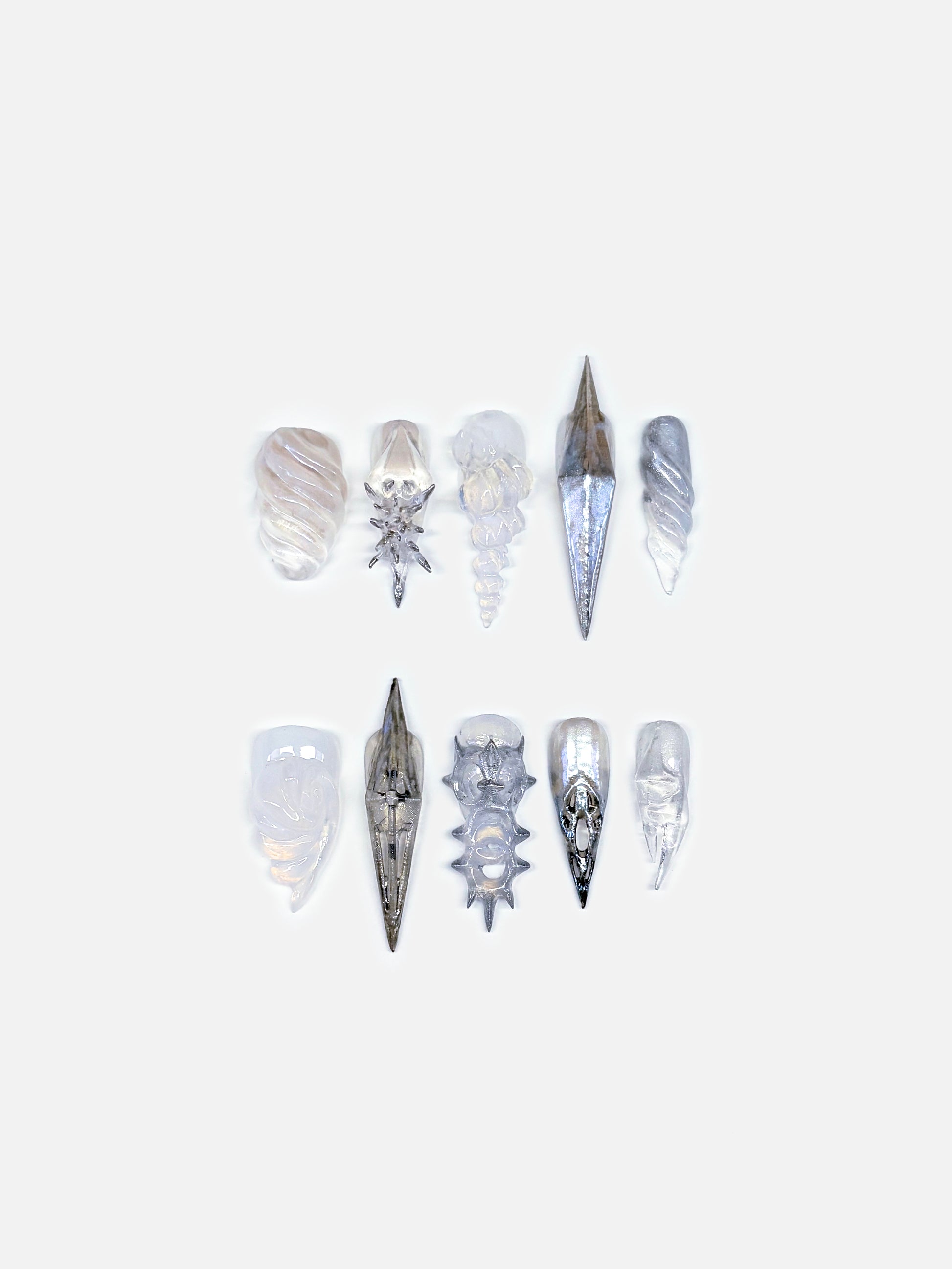 Close-up of silver sculptural 3D shell nails, metallic gradients. Each form feels like ocean armor reborn, a poetic fusion of flower nail art and conceptual design. The texture and depth capture the interplay between organic evolution and futuristic craftsmanship, presenting wearable art that transcends ordinary beauty.