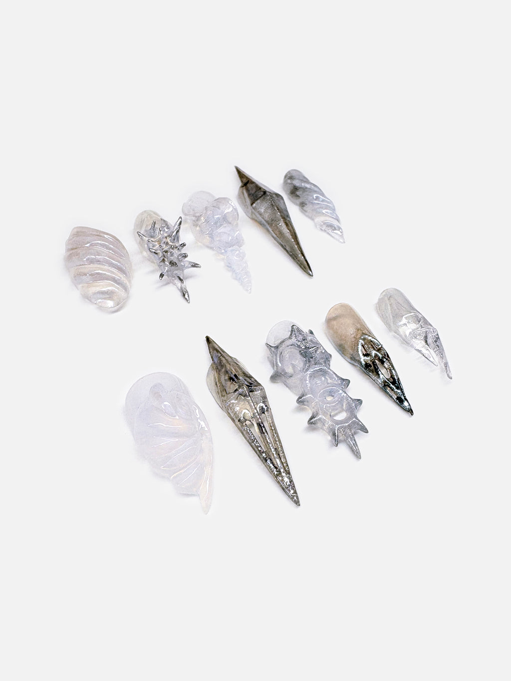 A futuristic 3D nail art set inspired by seashell armor, crafted in metallic silver and pearlescent white. Each sculptural press-on nail mimics the spiral and ridge of marine shells.