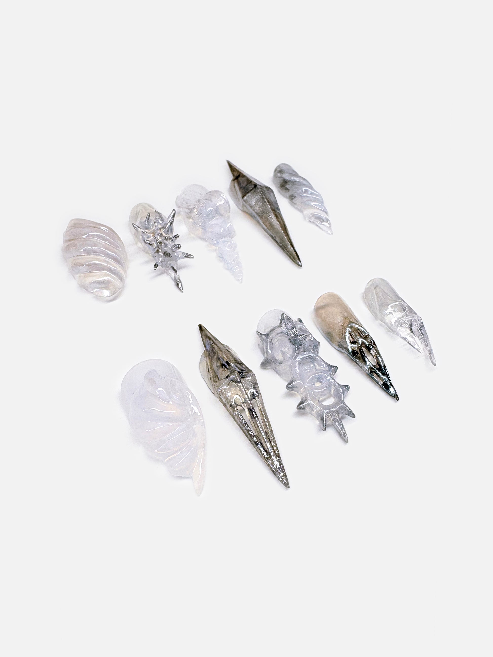 A futuristic 3D nail art set inspired by seashell armor, crafted in metallic silver and pearlescent white. Each sculptural press-on nail mimics the spiral and ridge of marine shells.