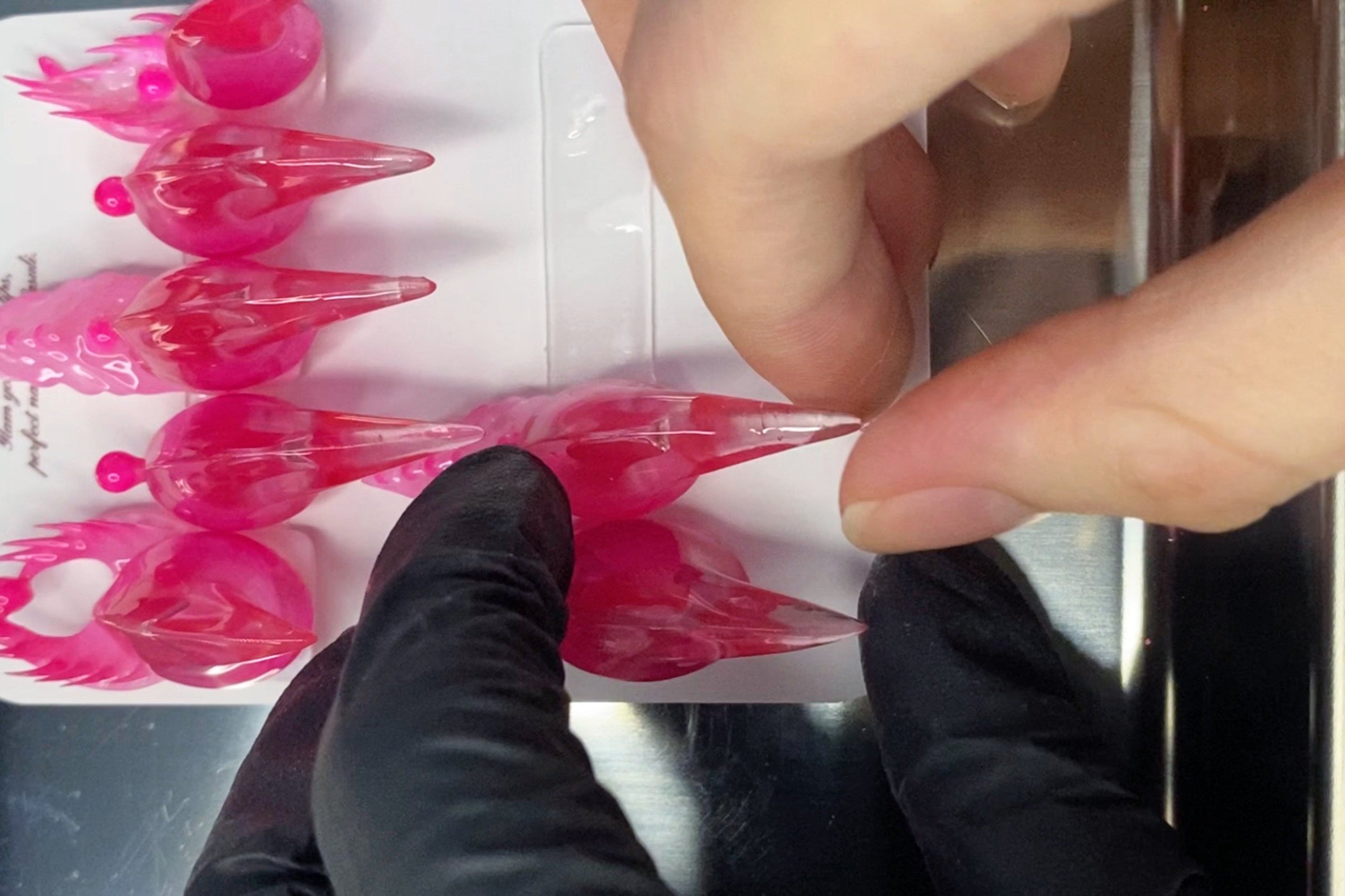 hand placing a piece of nail in the storage sheet, where there are already 7 pieces fake nails on the sheet.
